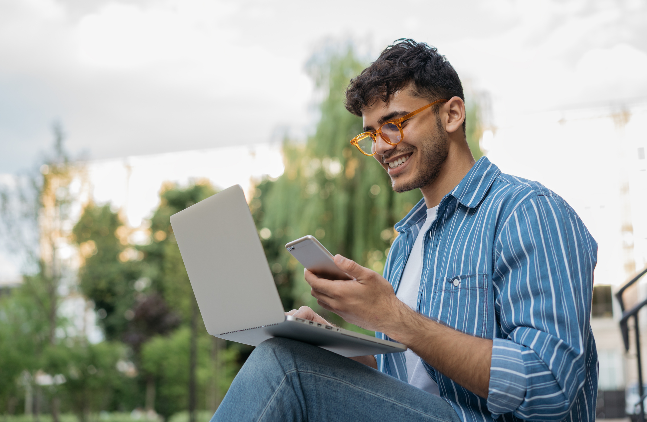 Image of man using a laptop while smiling and holding his phone.